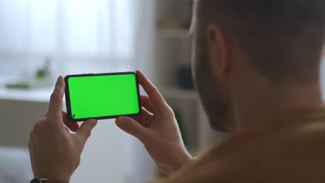 man-is-viewing-on-green-screen-of-mobile-phone-holding-horizontally-modern-gadget-and-app-for-education-communication-and-entertainment-closeup-view